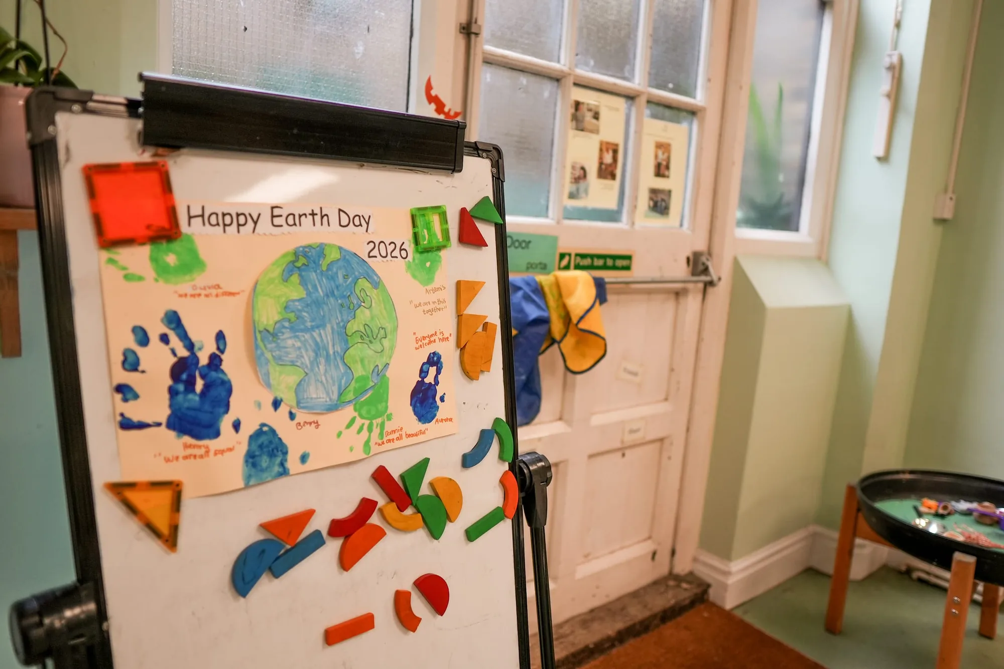 A Happy Earth Day 2026 poster with children’s handprints and magnetic shapes