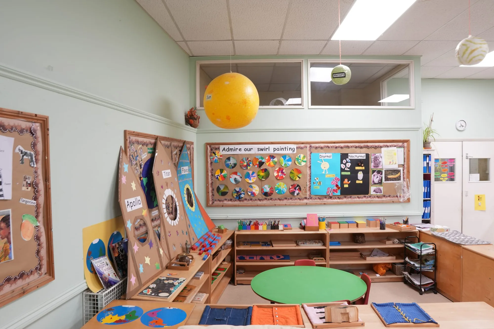 A hanging Sun and Mercury above cardboard rockets, swirl paintings and Montessori shelves
